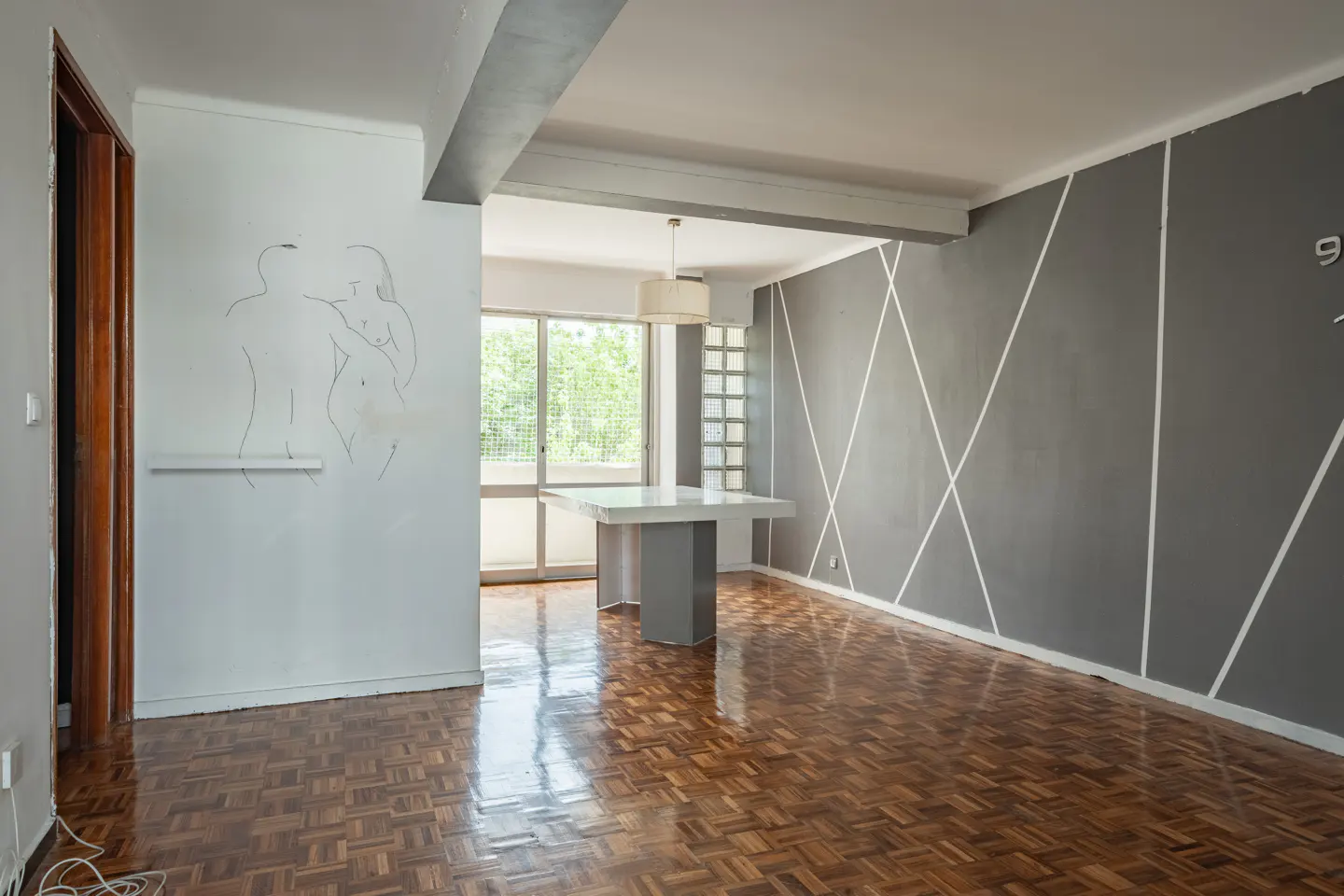 A modern apartment interior with parquet floors, gray walls with white stripes, and a white table near a window.