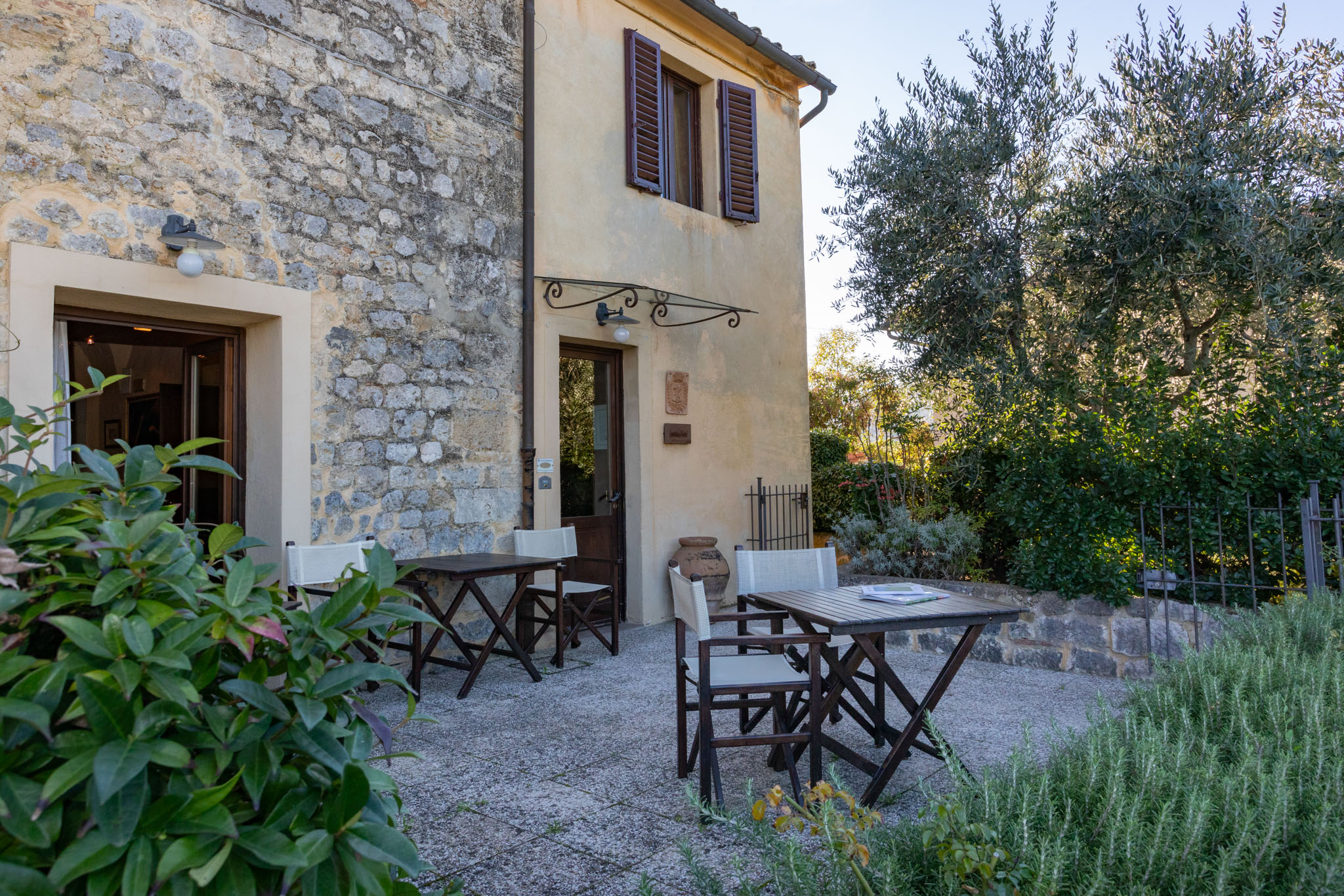 Exterior view of a stone building with tables and chairs on a patio, surrounded by greenery.