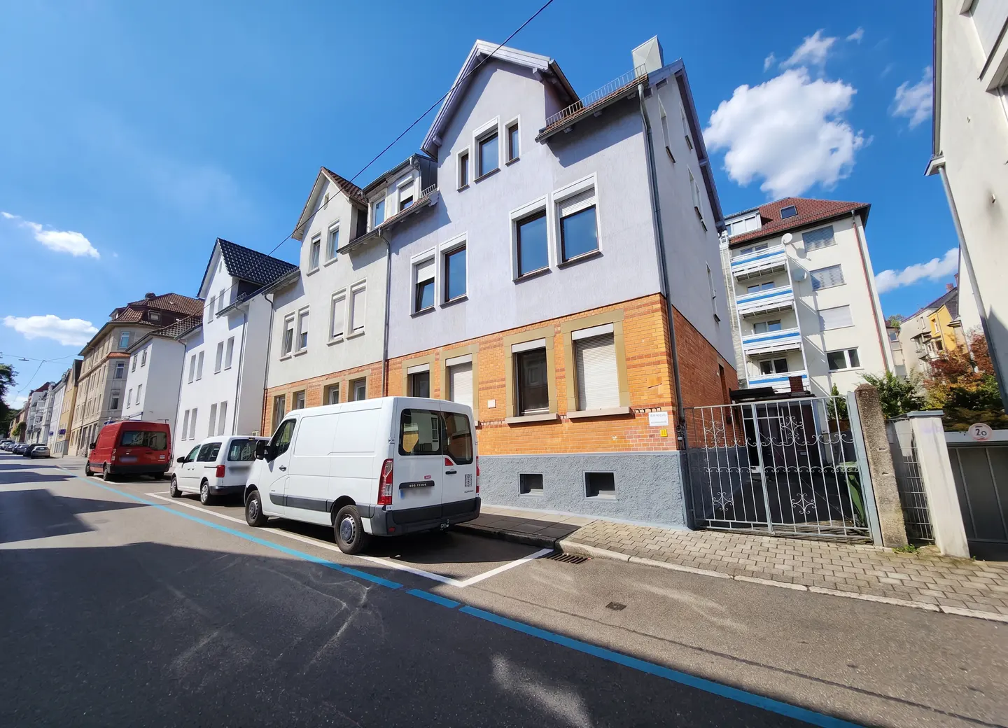 Street view of a row of buildings, with a white van parked on the side of the road on a sunny day.