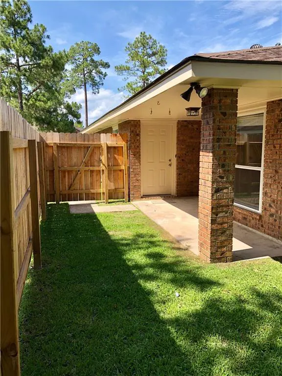 Backyard view of a brick home with a covered patio, white door, and a wooden privacy fence under a blue sky.