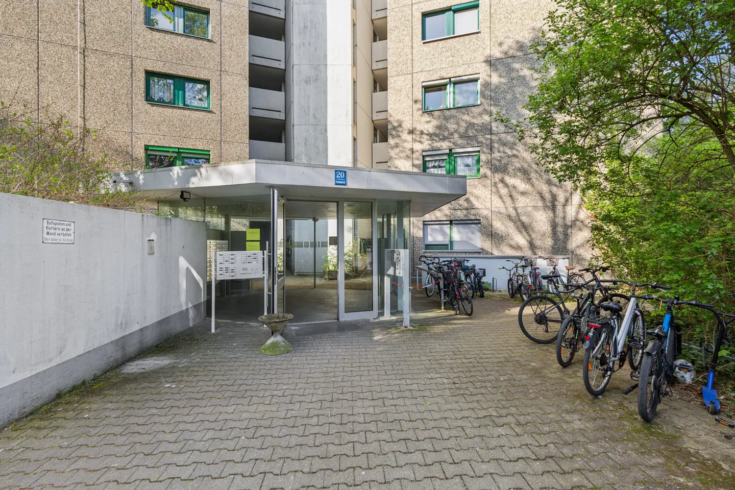 Apartment building entrance with glass doors and a bike rack. The building is concrete with green window frames.