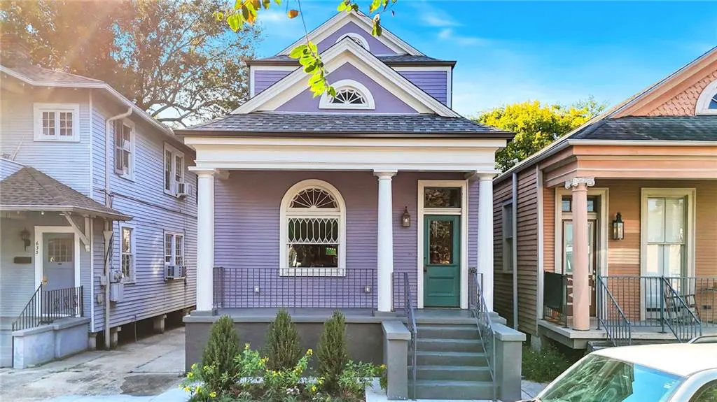 A lavender house with a green door and white columns, with a small yard and steps leading to the front porch.