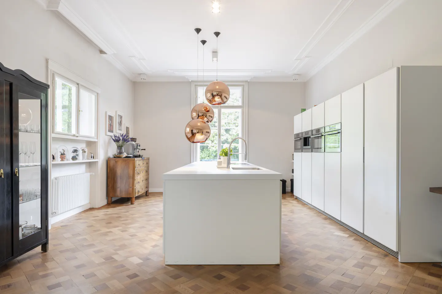 Bright kitchen with white cabinets, island, and herringbone wood floors. Copper pendant lights hang above the island.