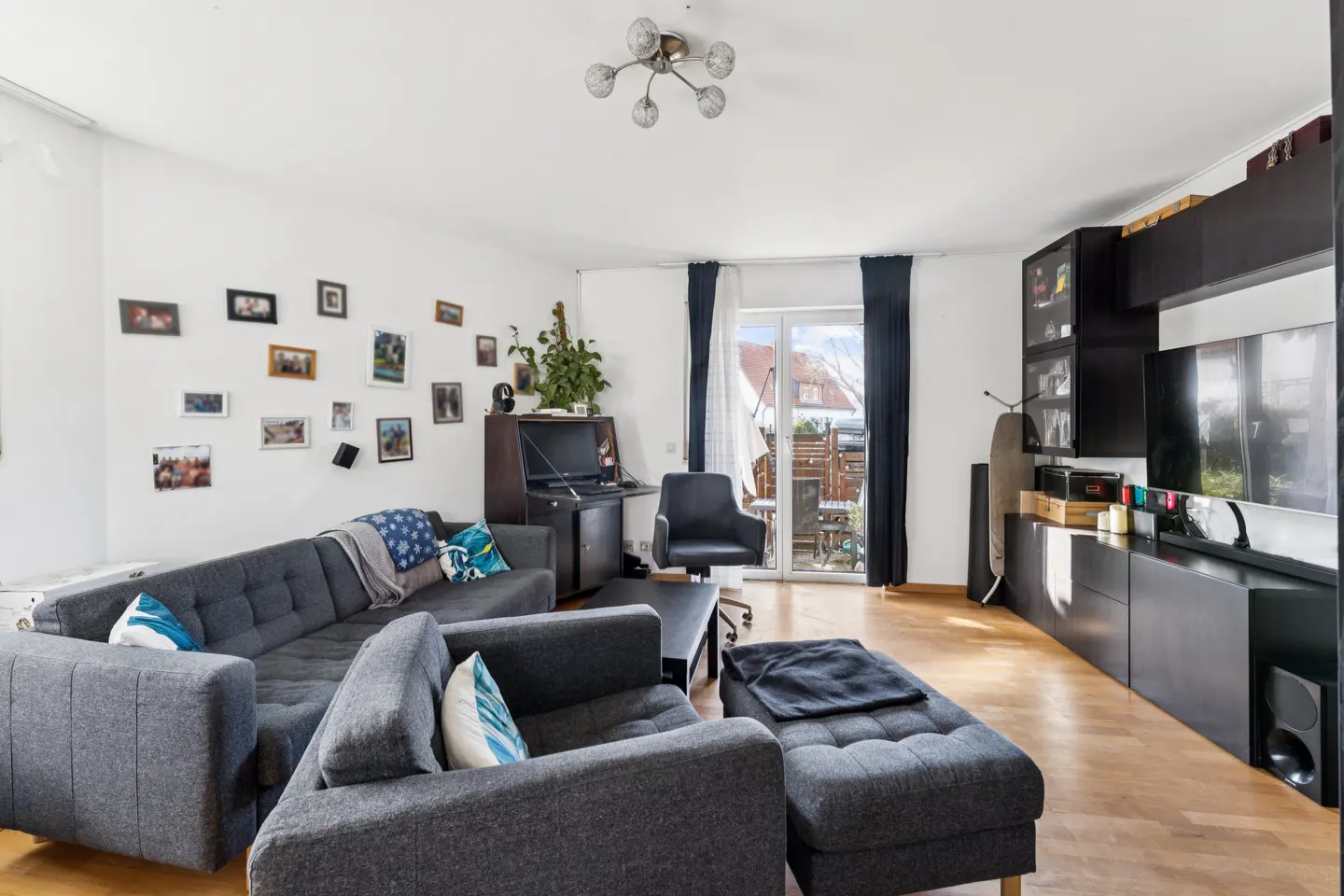 Living room with grey sectional sofa, matching ottoman, gallery wall, dark media unit, and glass door to a patio.