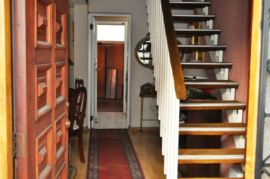 Open wooden front door reveals a hallway with stairs, a red rug, and a doorway leading to another room.