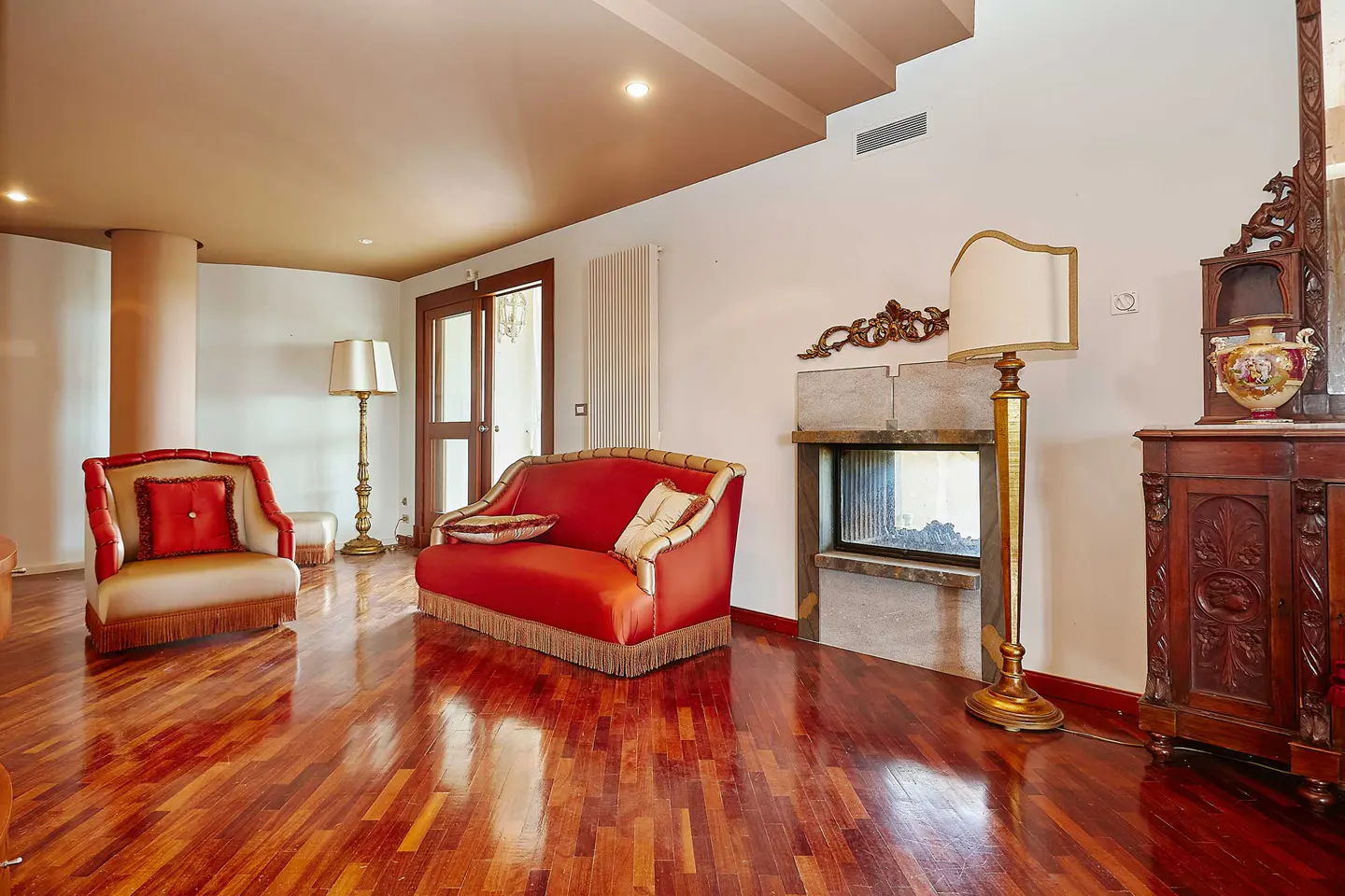 A living room with a red sofa, armchair, fireplace, and hardwood floors.