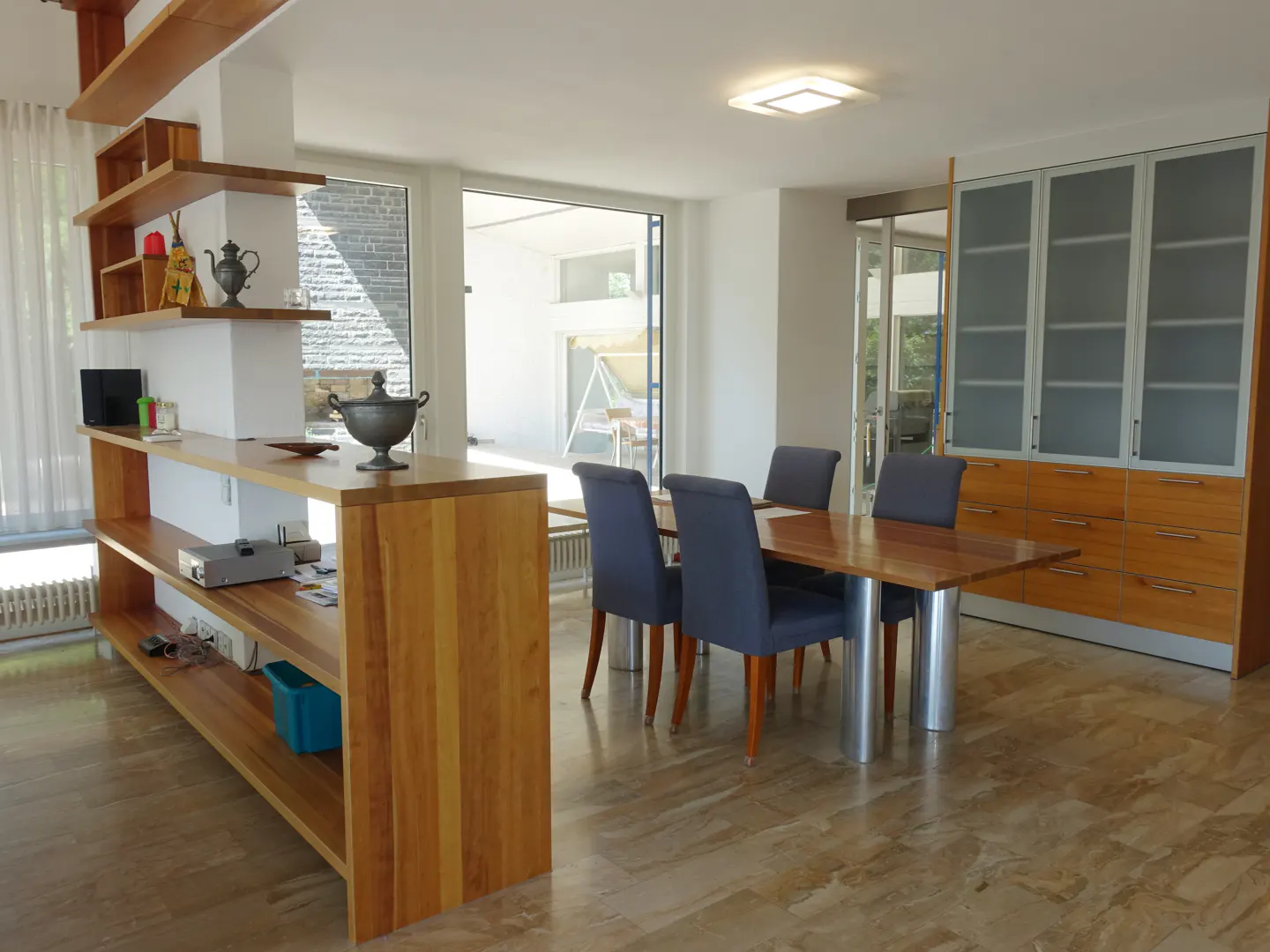 A modern dining room with a wood table, blue chairs, and built-in shelving and cabinets.