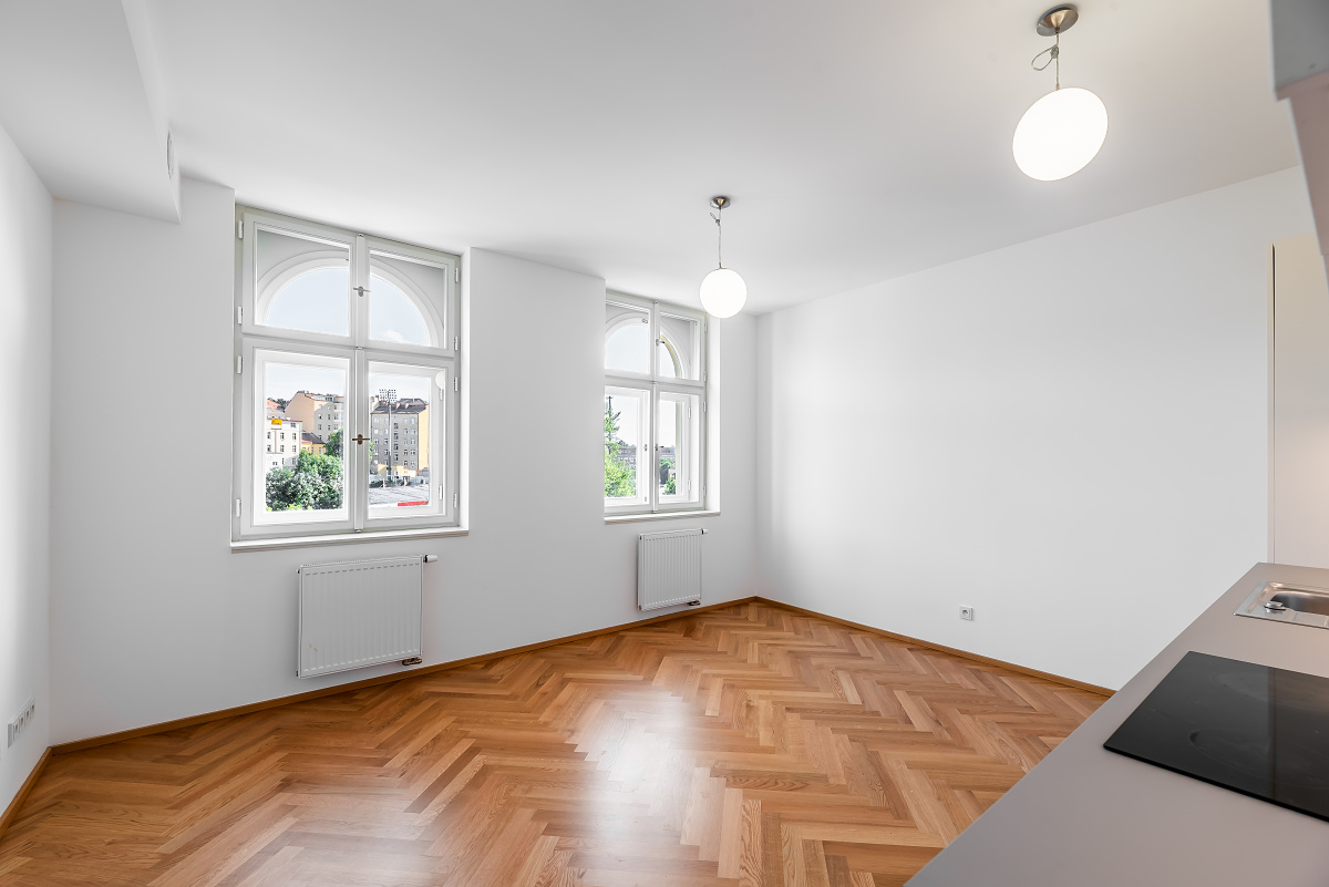 Empty room with white walls, herringbone wood floors, two arched windows, and modern pendant lights. [AI-generated text]
