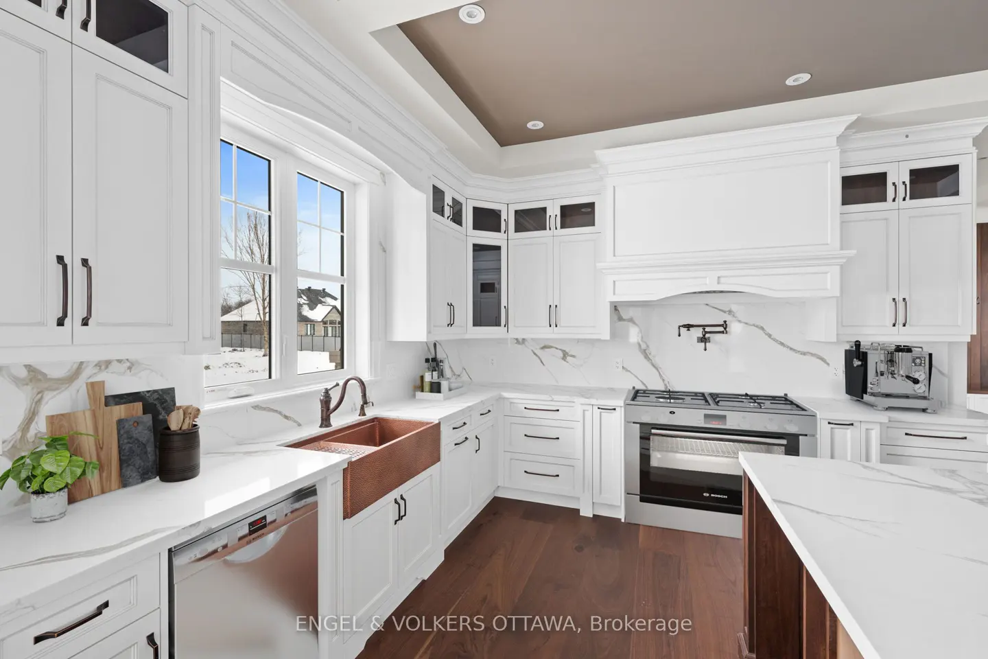 Bright kitchen with white cabinets, marble countertops, and a copper sink. Stainless steel appliances and dark wood floors add contrast.