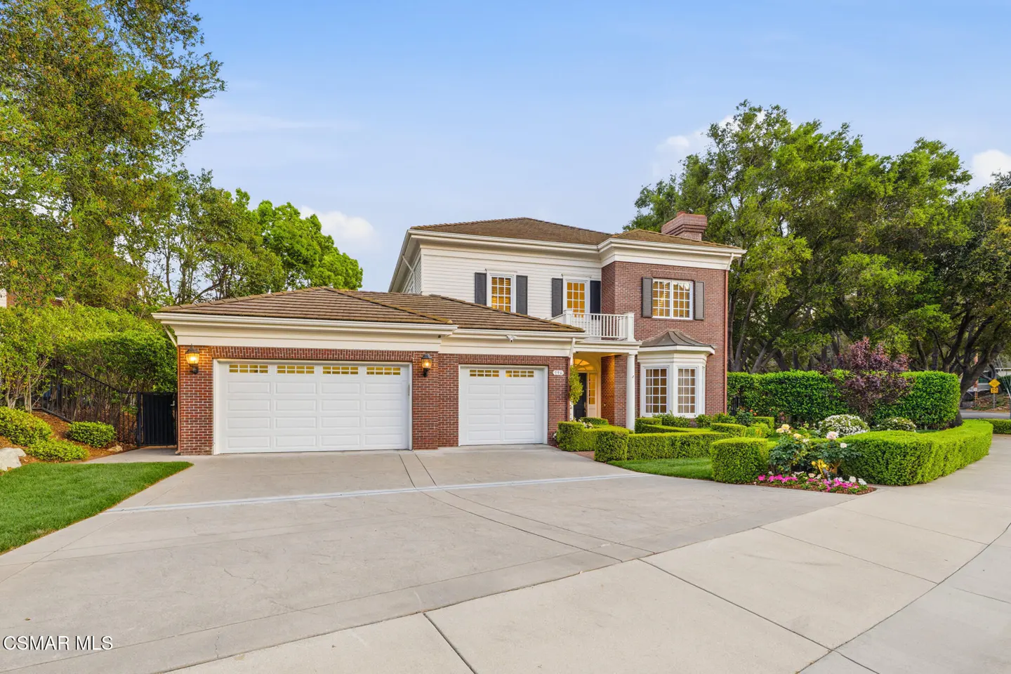 Two-story brick and white house with a three-car garage, manicured lawn, and blue sky.