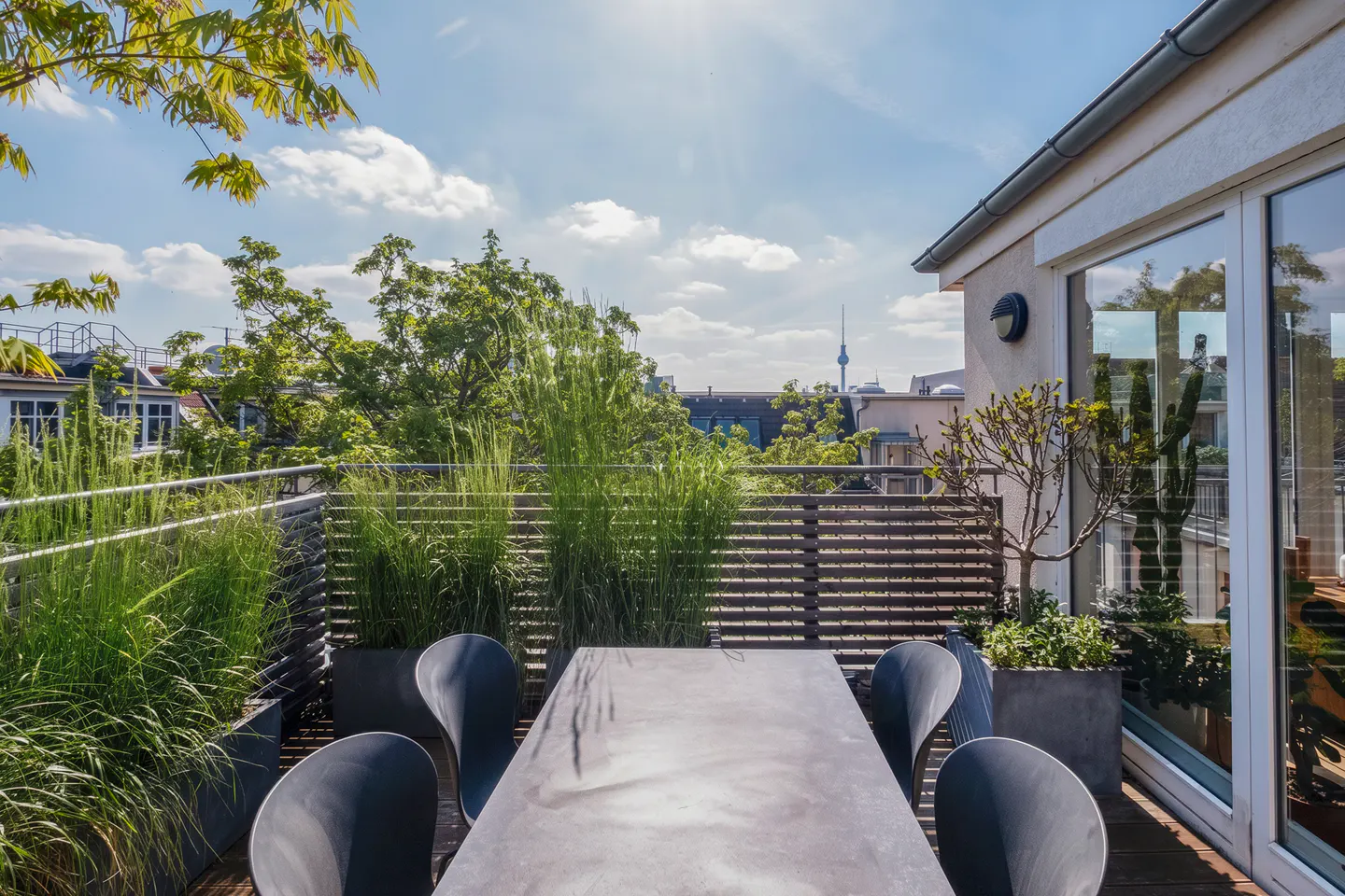 A rooftop patio with a gray table and chairs, potted plants, and a view of the city skyline.