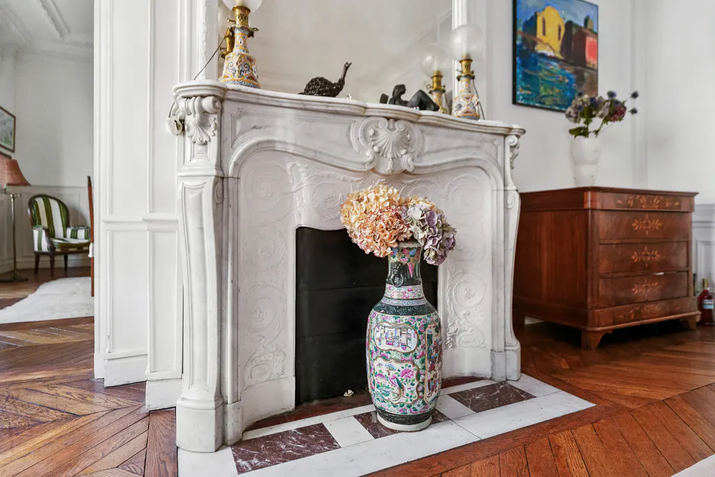Living room with a white marble fireplace, a colorful vase with flowers, and a wooden dresser with a painting above it.