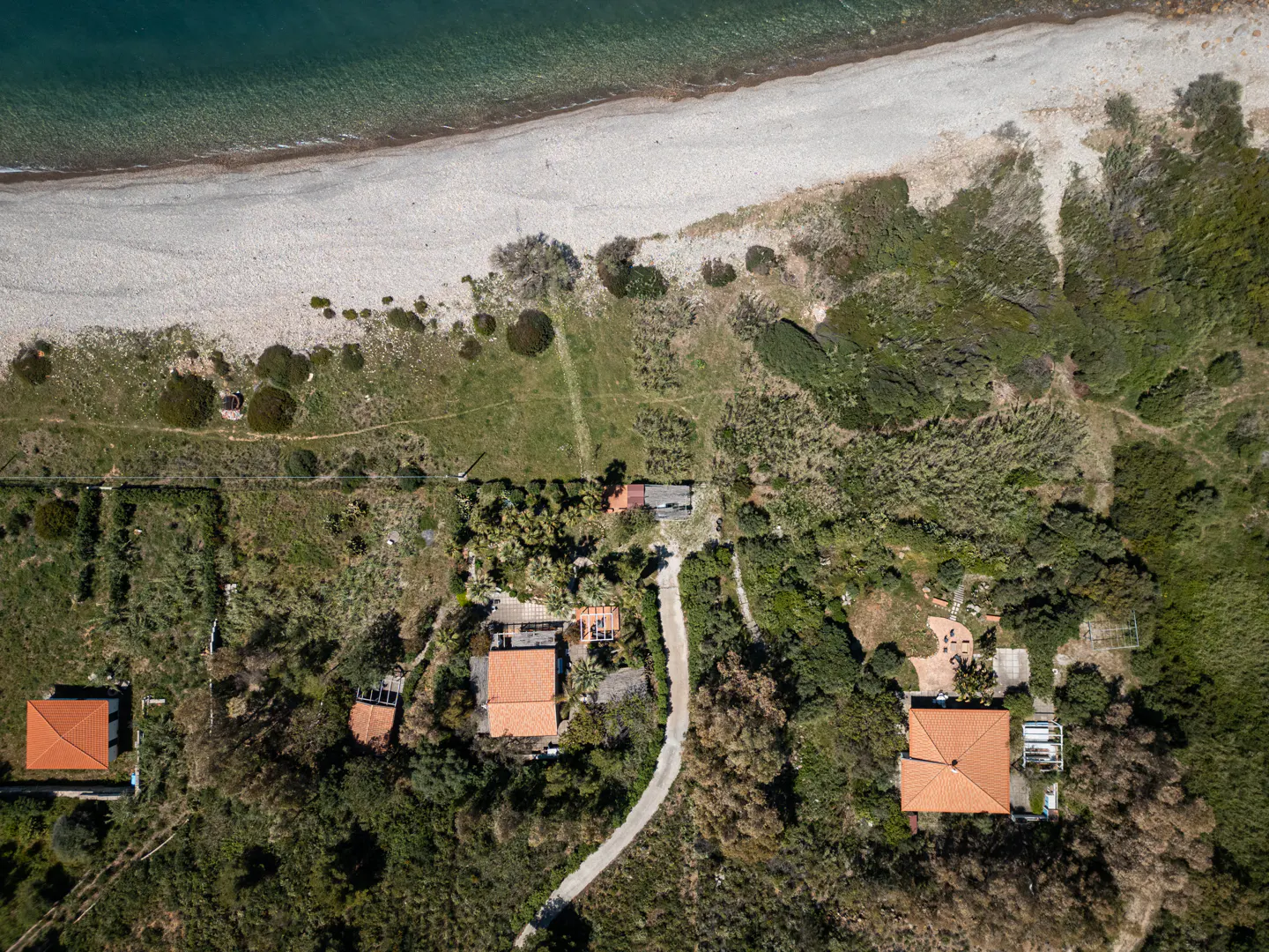 Aerial view of houses with orange roofs near a beach with green vegetation and blue water.