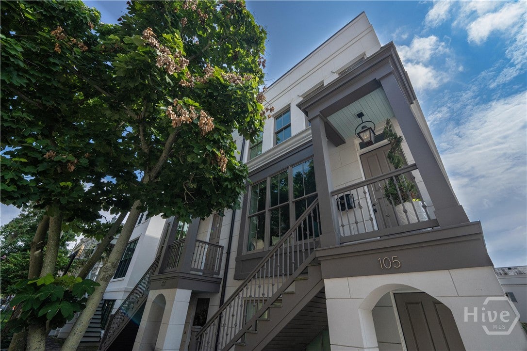 Low-angle view of a modern white townhouse with dark grey trim, an elevated front porch, and a large tree in the foreground. [AI-generated text]