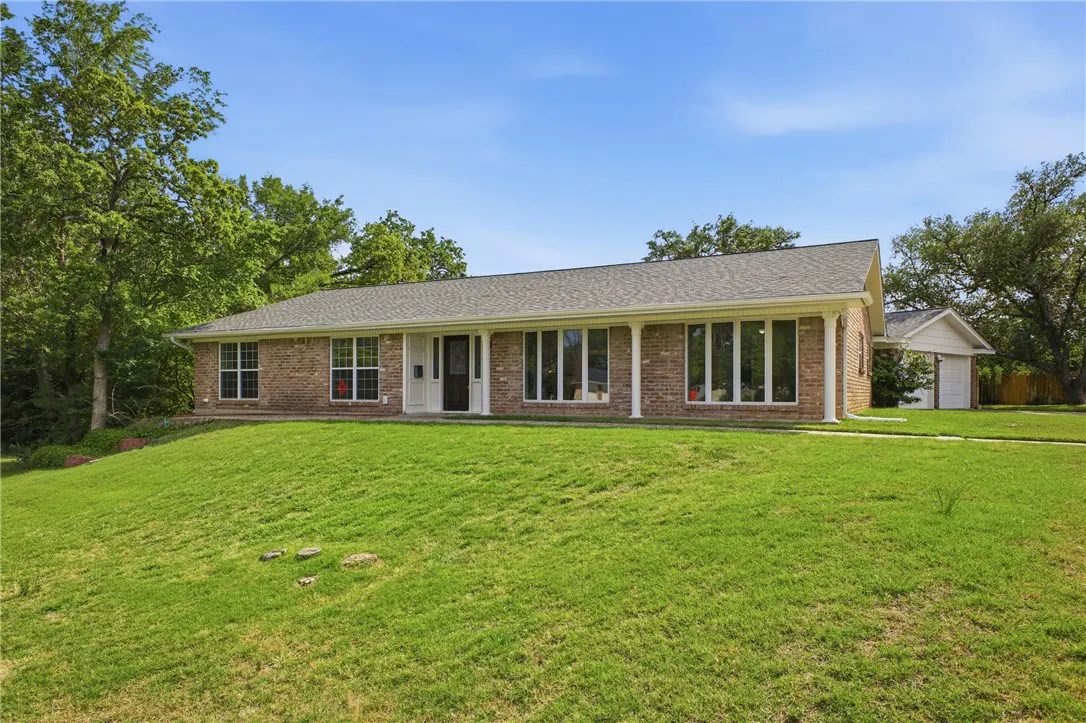Brick ranch-style home with a black door, white trim, and a green lawn under a blue sky.