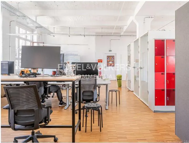 Bright, open office space with desks, chairs, and red lockers. Wood floors and white walls create a modern, airy feel.