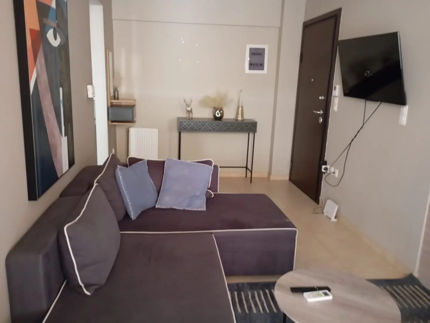 Living room with a brown sectional sofa, blue pillows, a black console table, and a mounted TV on a gray wall.