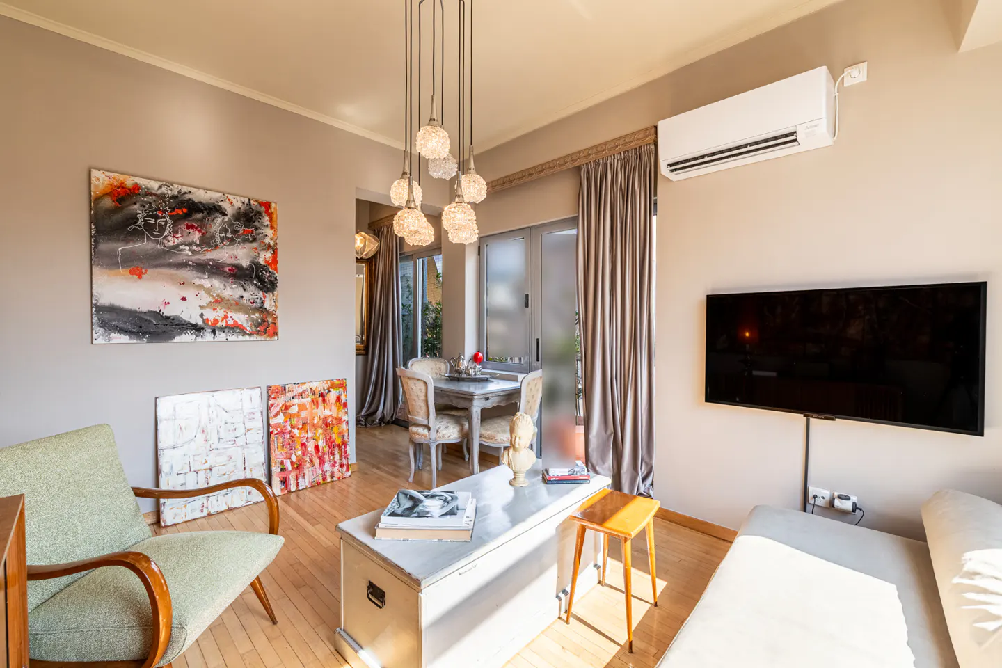 Modern living room with a green armchair, white storage chest, wall-mounted TV, and a dining area with a pendant light.