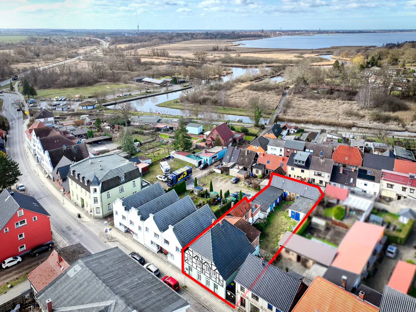 Aerial view of a half-timbered house with a red outline, located in a village near a lake and fields.