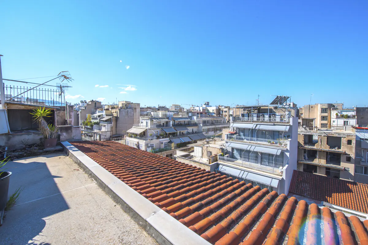 View from a rooftop with red tile roofs, overlooking a city with white buildings under a clear blue sky.