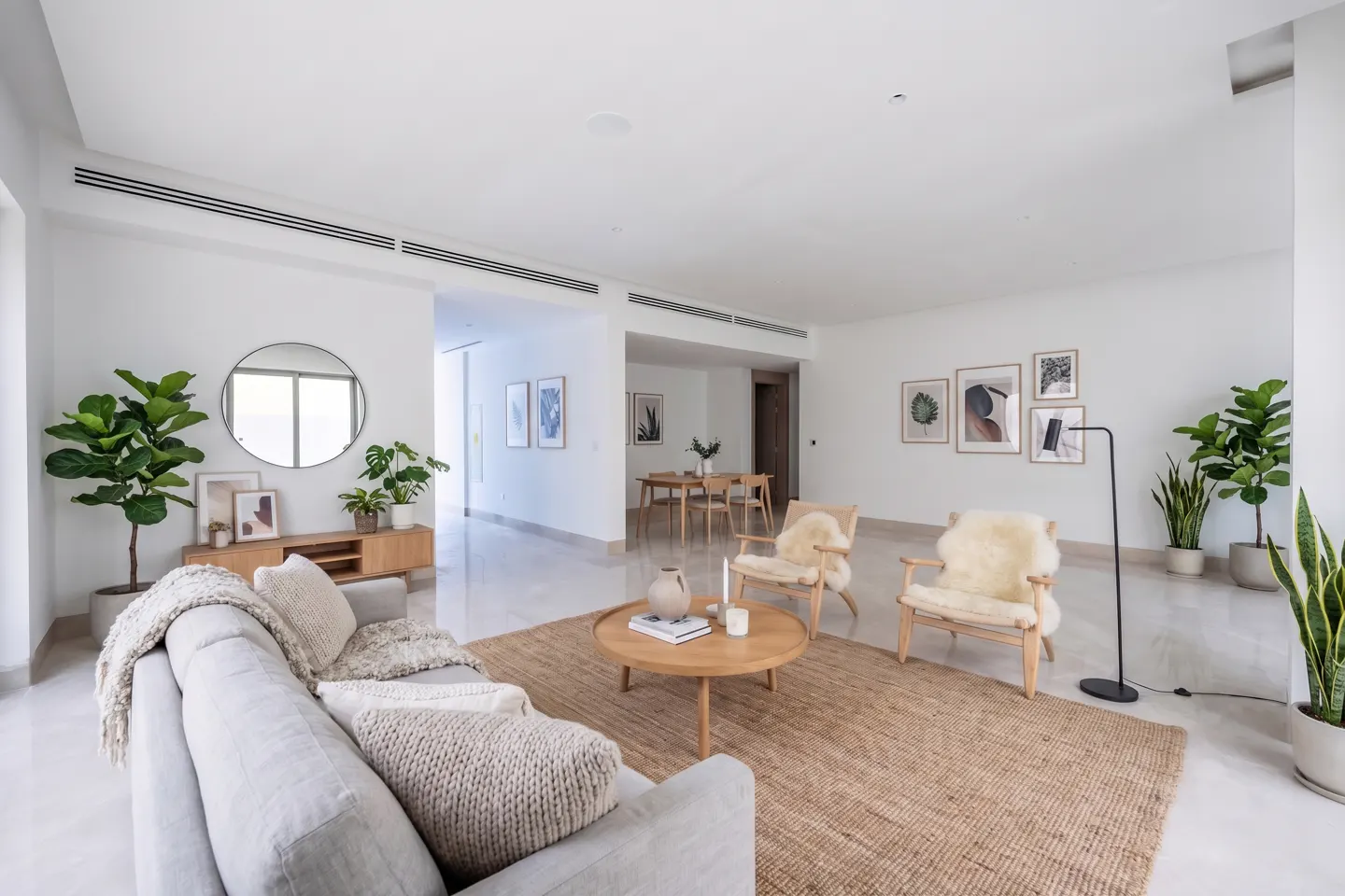 Bright, open living room with a gray sofa, jute rug, and wooden furniture. Plants and artwork add a touch of nature to the white walls.