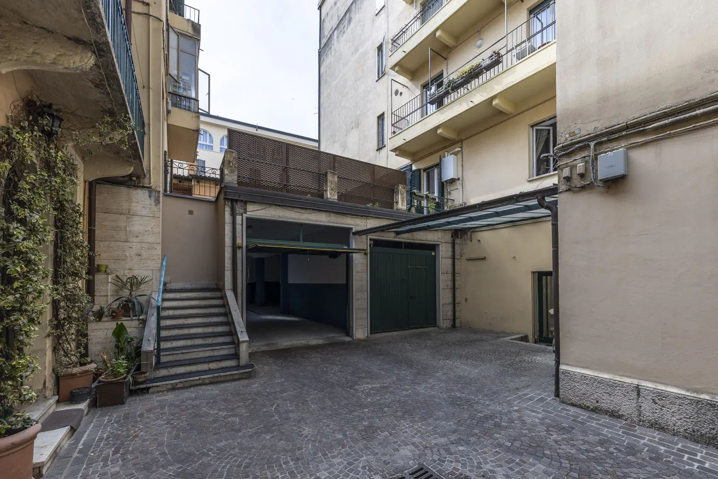 A courtyard with two garages, one with an open door, and a staircase leading to an upper level.