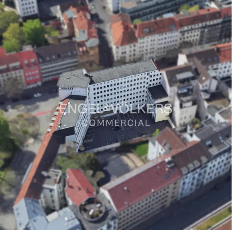 Aerial view of a white commercial building with a parking lot, surrounded by other buildings with red roofs.