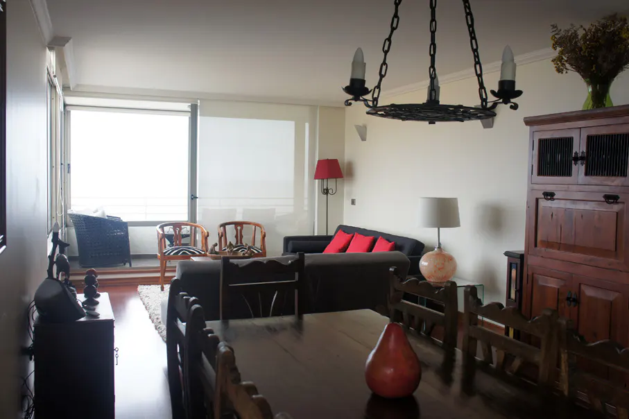 Living room with dark wood dining table, chairs, and hutch. A black sofa with red pillows sits near a window. A black chandelier hangs above.