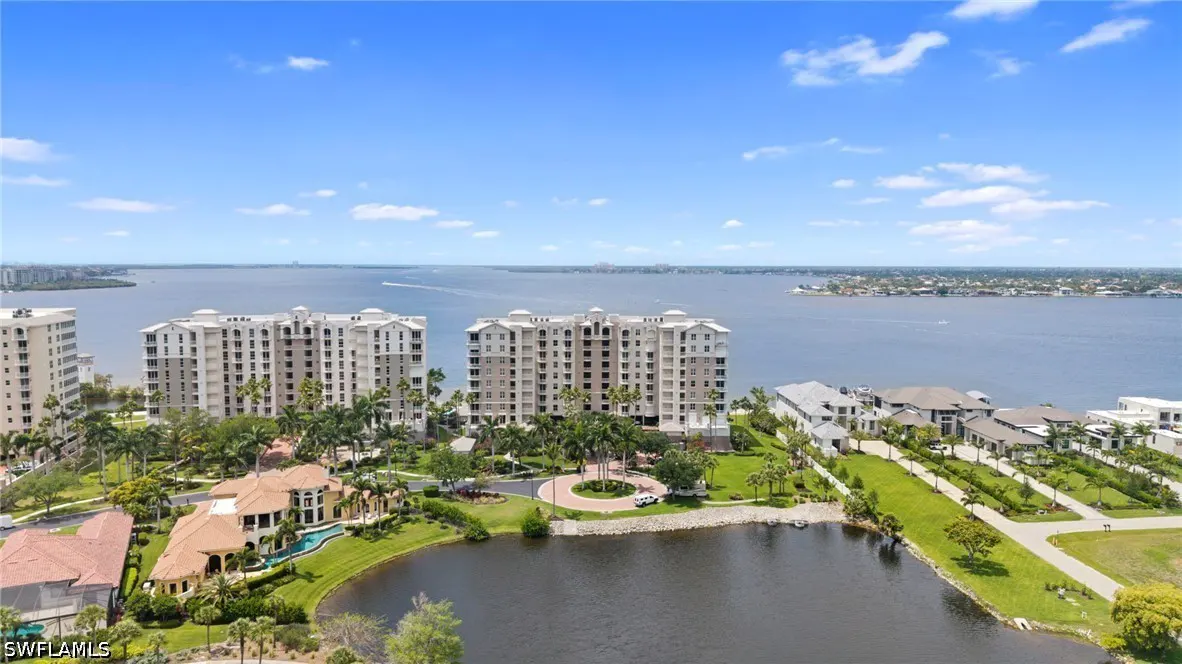 Aerial view of waterfront condos and luxury homes. Blue sky, water, and green landscaping.