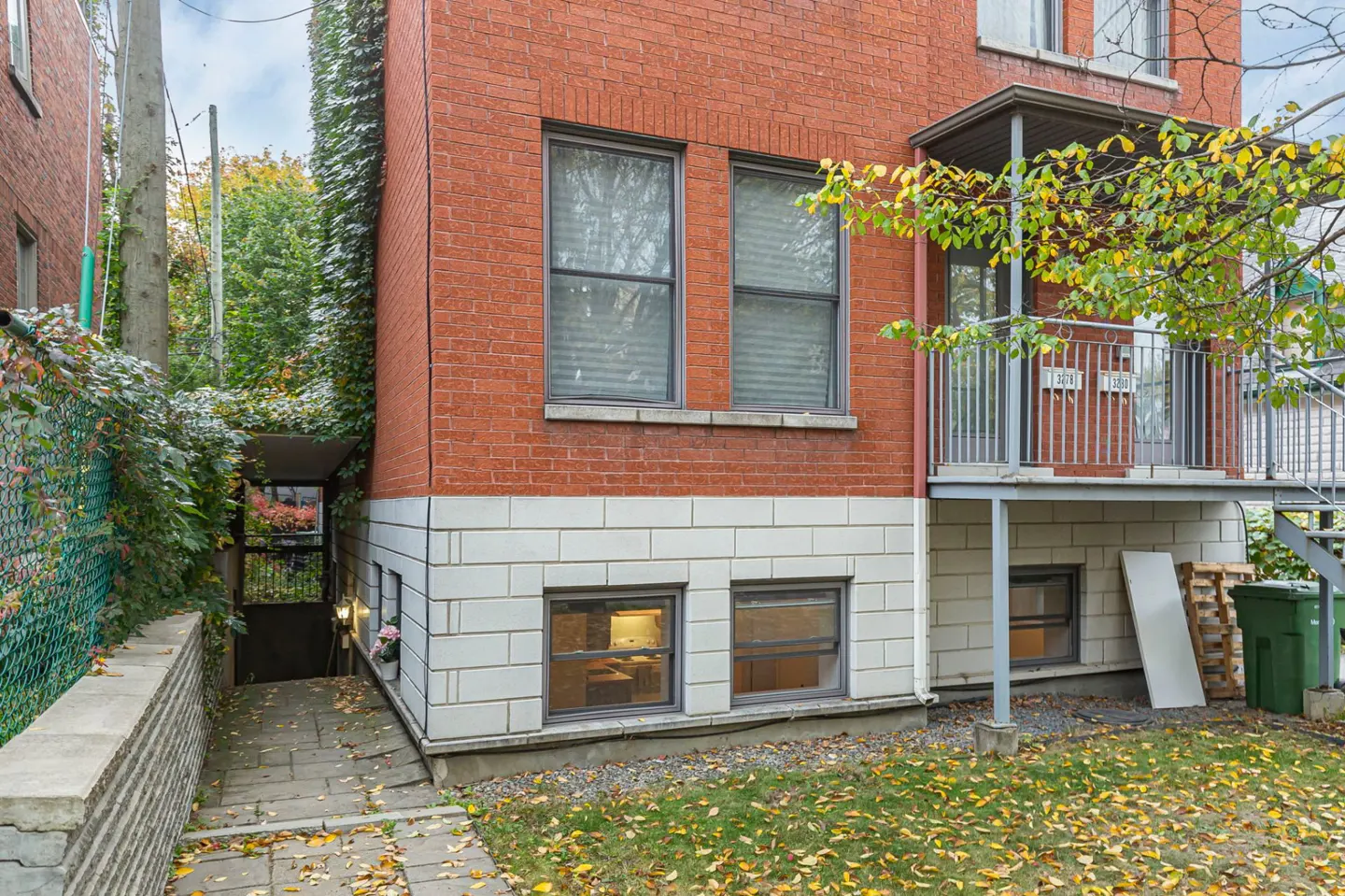 Exterior view of a red brick apartment building with a stone walkway leading to a covered entrance and a metal balcony.