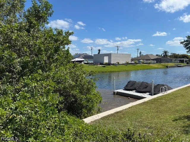 Waterfront property view with a dock, covered jet skis, and a canal under a blue sky with scattered clouds.