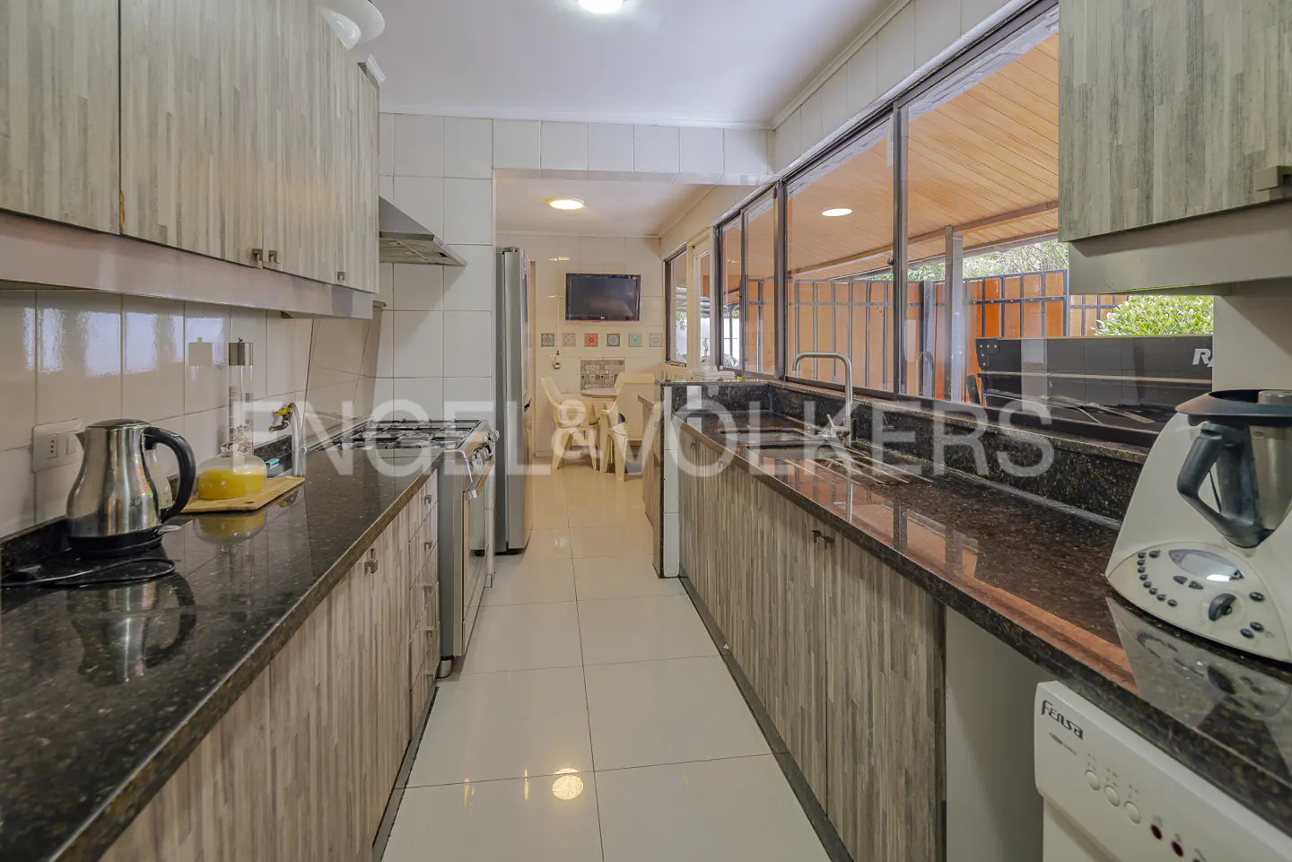 Galley kitchen with wood-grain cabinets, dark granite countertops, stainless steel appliances, and a view of a patio.
