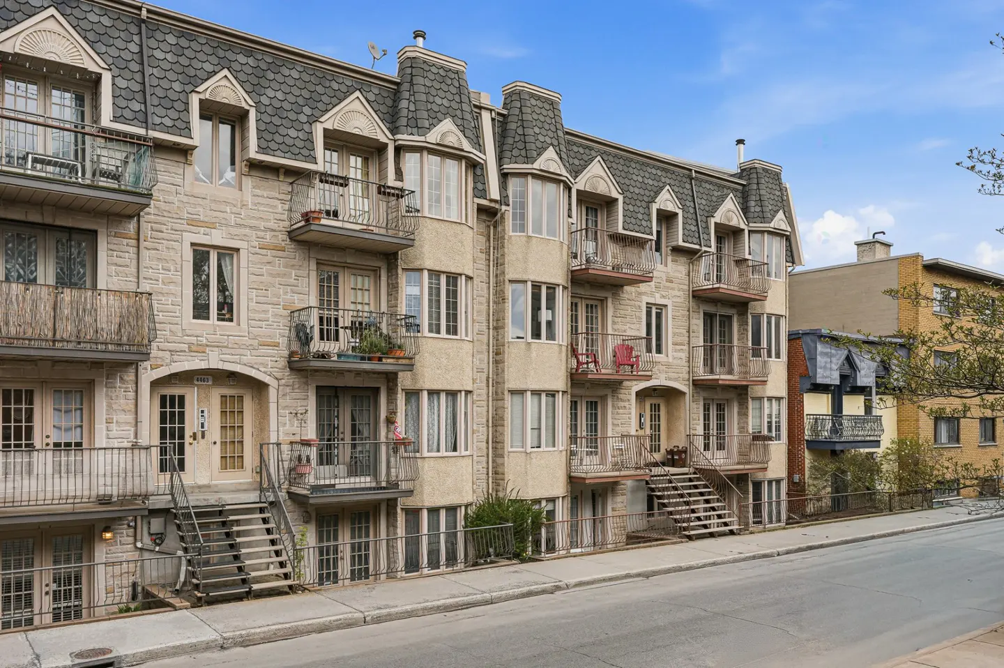 Exterior view of a multi-story apartment building with balconies and stone facade under a blue sky.