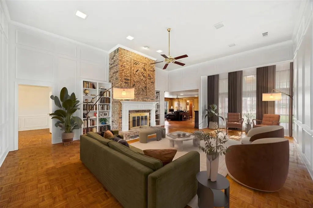 Bright living room with hardwood floors, white walls, and a brick fireplace. A green sofa and brown chairs provide seating.
