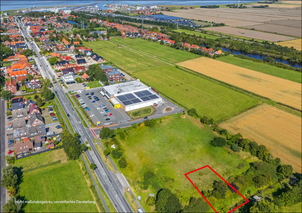 Aerial view of a town with a red-outlined vacant lot next to a commercial building, green fields, and a nearby road.