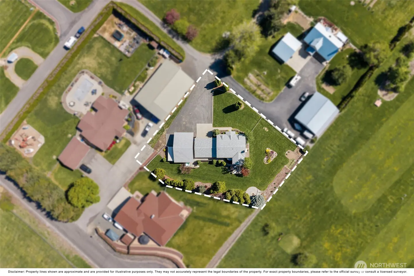 Aerial view of a single-story house with a gray roof, surrounded by green lawn and a white dashed property line.