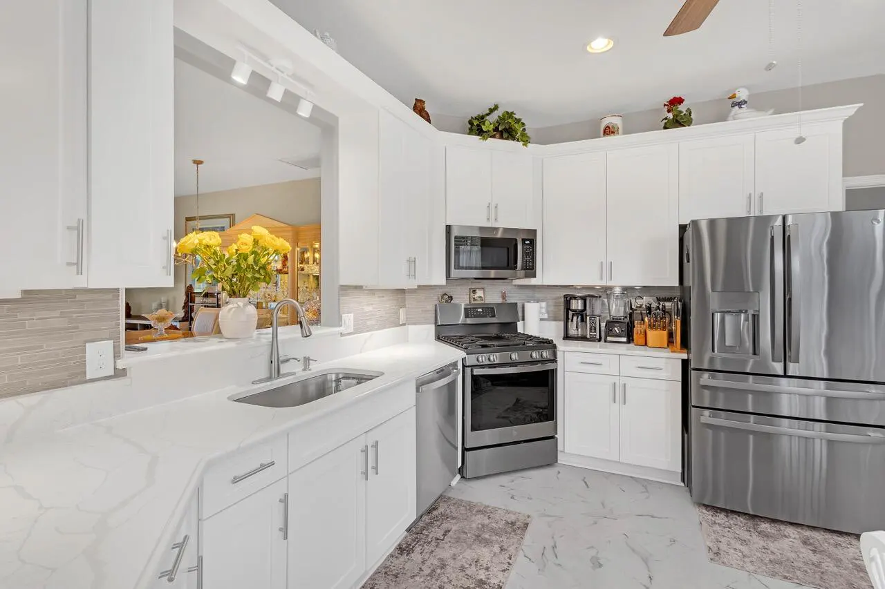 Bright kitchen with white cabinets, marble countertops, and stainless steel appliances. Yellow flowers add a pop of color.
