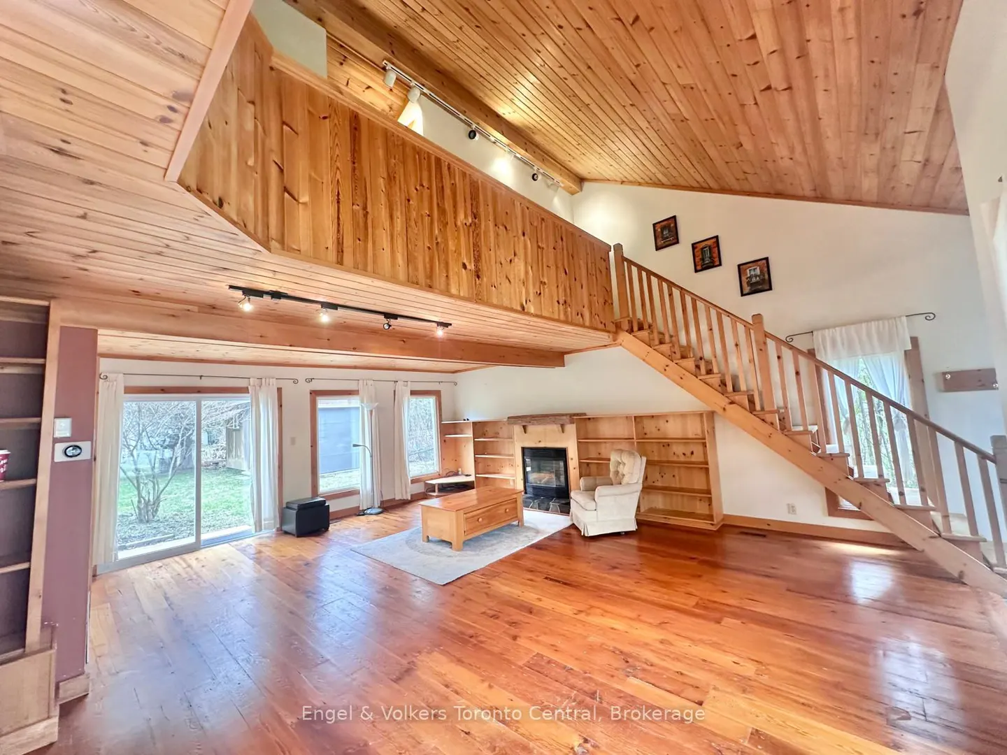 A spacious living room with wood floors, a fireplace, and a staircase leading to a loft.