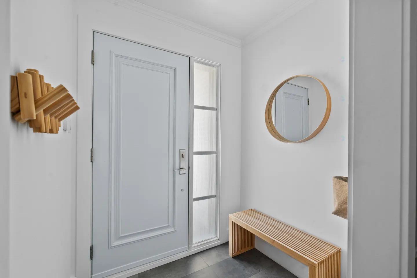 Entryway with a white door, sidelight, and wooden bench. A round mirror hangs above the bench. A wooden coat rack is on the left wall.