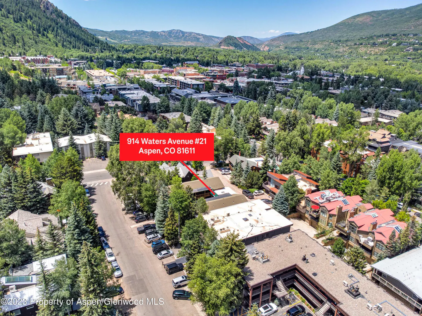 Aerial view of 914 Waters Avenue #21, Aspen, CO, surrounded by green trees and mountains in the background. Cars parked on the street.