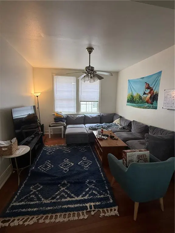 Living room with a large gray sectional sofa, blue patterned rug, and a light blue chair. A ceiling fan hangs above.