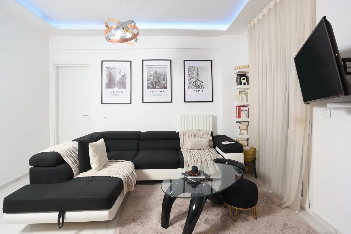 Bright living room with a black and white sectional sofa, glass coffee table, and framed city prints on the wall.
