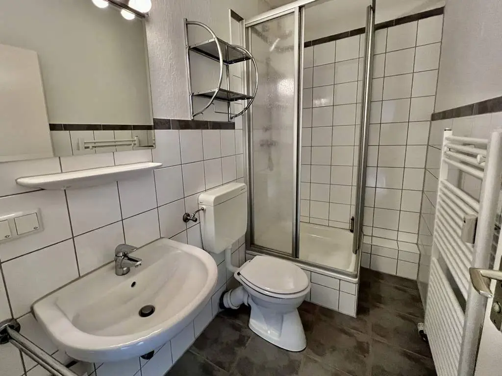 A bathroom with white tiled walls, a sink, toilet, and glass-enclosed shower.