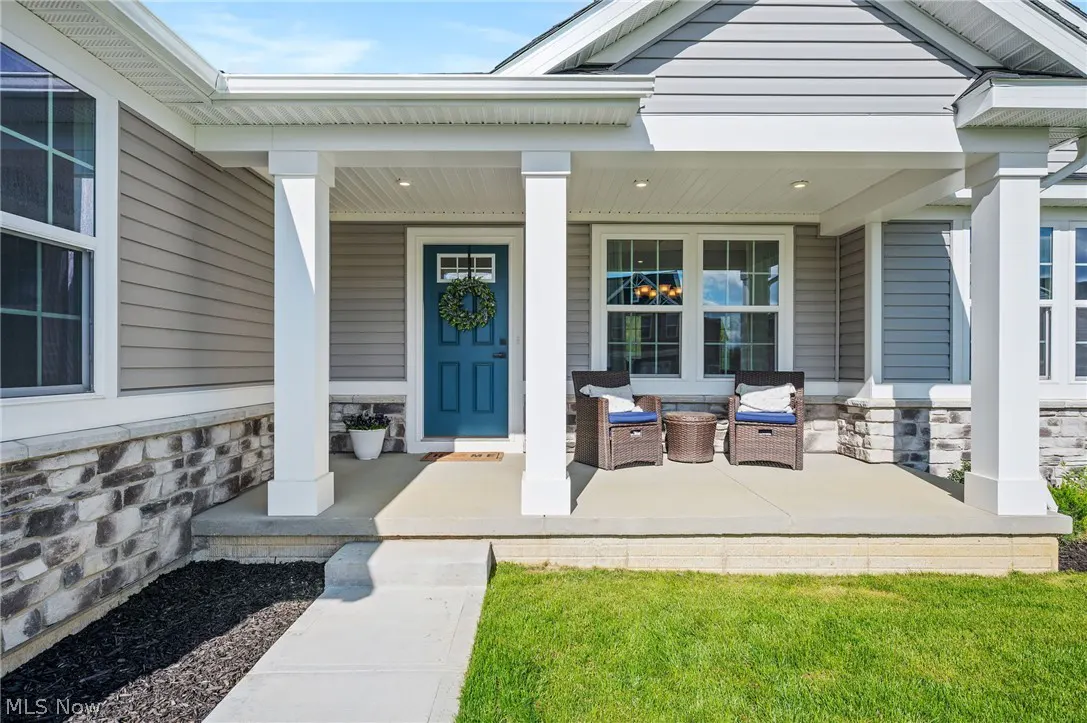 Home exterior with a covered porch, blue door with wreath, and two chairs.