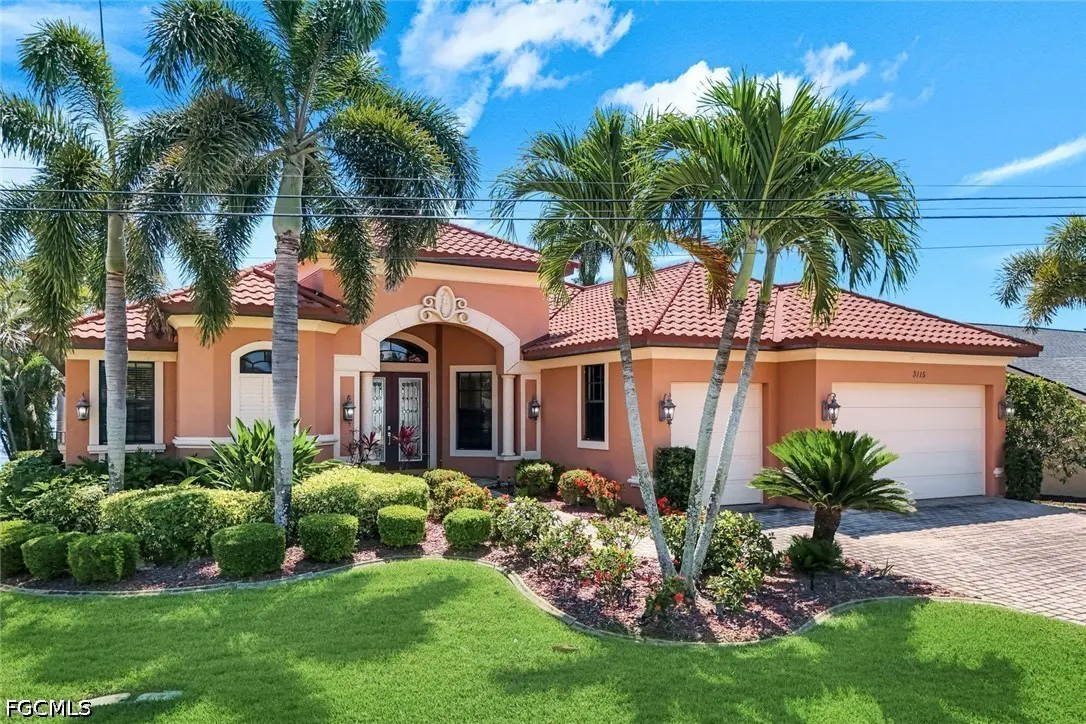 A salmon-colored house with a red tile roof, palm trees, and a green lawn under a blue sky.