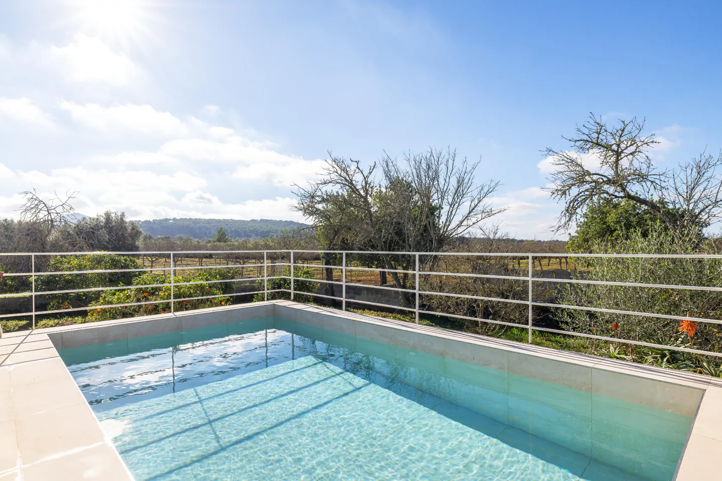 Outdoor pool with clear blue water, surrounded by a white fence, overlooking trees and a blue sky.