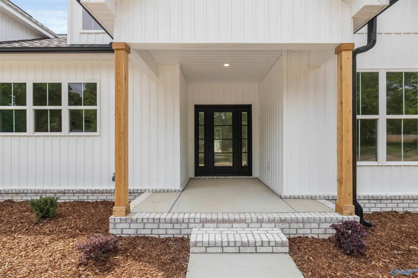 Front entrance of a white farmhouse-style home with a black front door and wooden support beams.