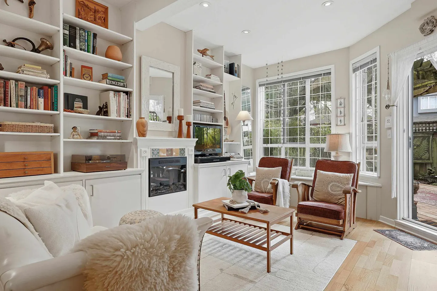 Bright living room with white built-in bookshelves, a fireplace, two leather armchairs, and a white sofa with a fur throw.