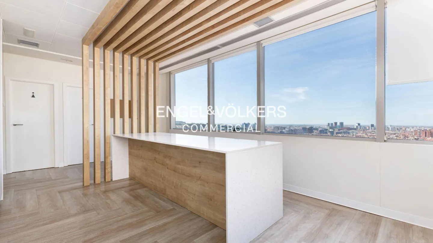 Office space with a white and wood reception desk, wood slat ceiling, and large windows with a city view. Engel & Völkers logo on the window.