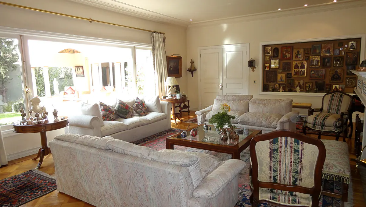 Bright living room with white sofas, wood floors, and a large window overlooking a garden. A gallery wall of icons adds character.